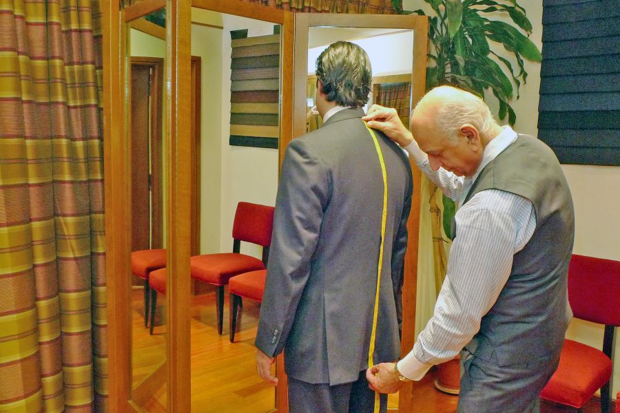 Lal Bhambi hand-cutting a bespoke suit pattern at Bhambi's Custom Tailors NYC – precise measurements for made-to-measure menswear